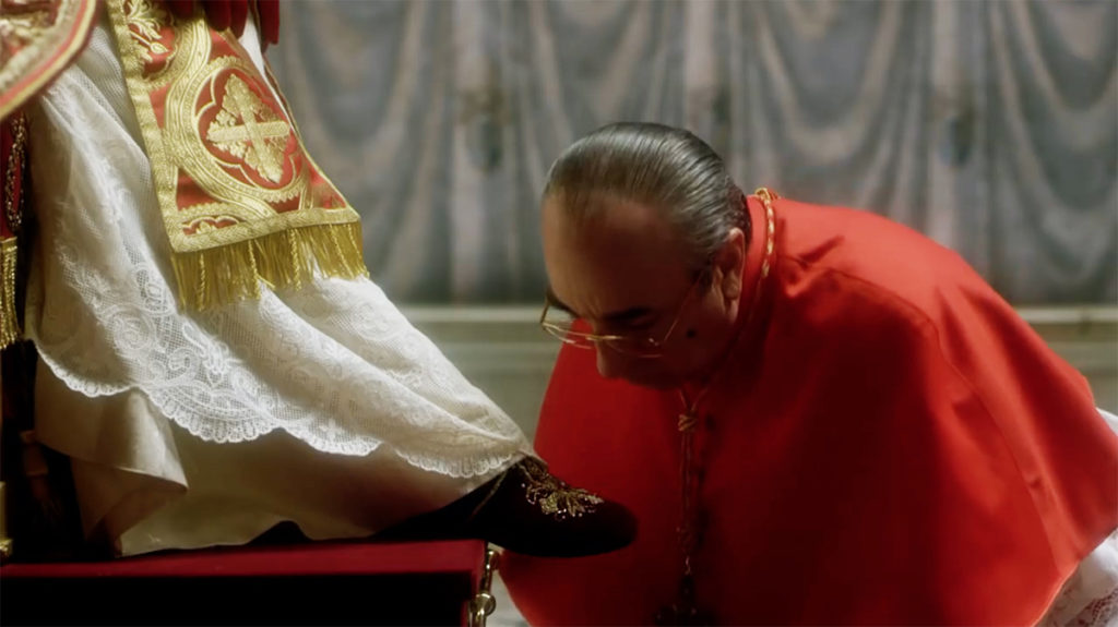Pie XIII, dans The Young Pope, est un tyran qui humilie ses conseillers, comme ici le cardinal Voiello (Silvio Orlando) en l'obligeant à baiser son pied, devant tous les autres cardinaux...